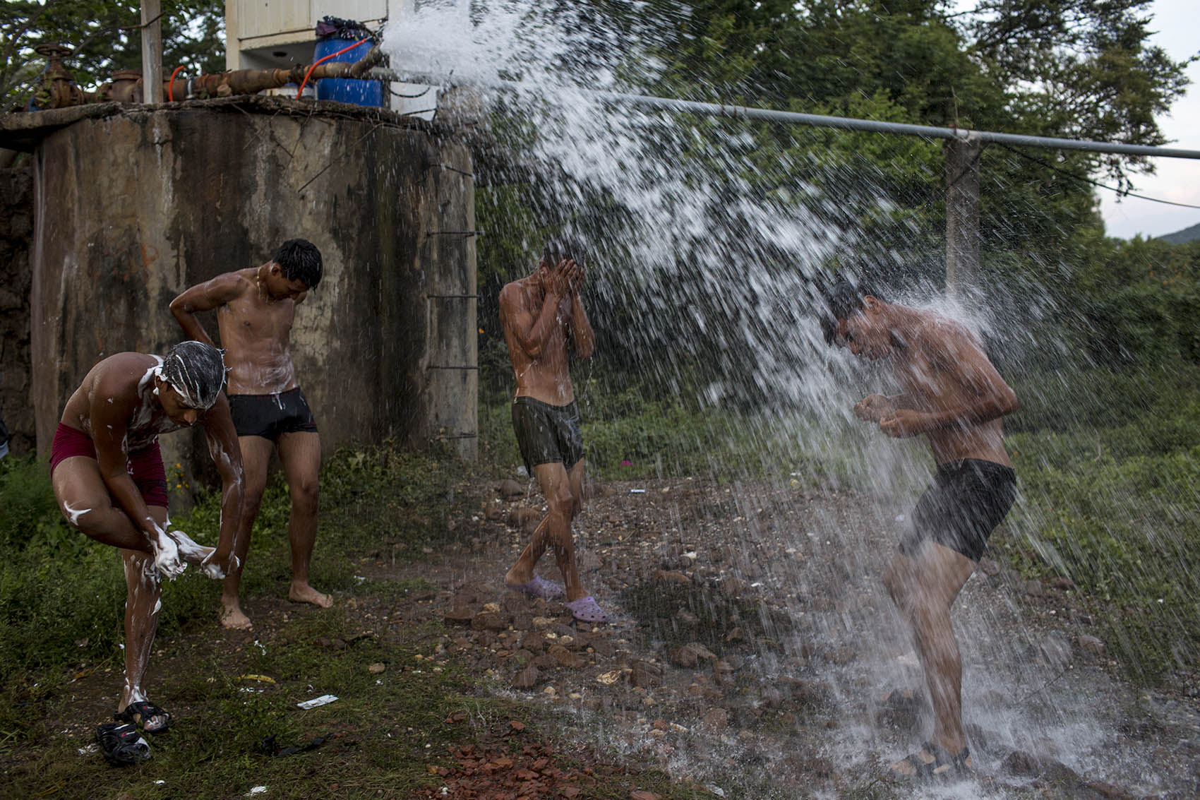 Jóvenes miembros de la barra brava del Olimpia, de Tegucigalpa, se duchan con el agua de una tubería, cerca del río de Niltepec / Simone Dalmasso