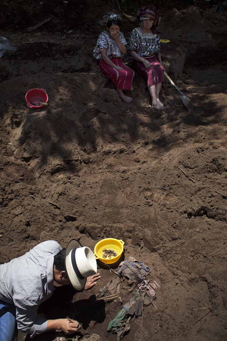 Un arqueólogo de la Fundación de Antropología Forense de Guatemala – FAFG – exhuma los restos de una mujer adulta bajo la mirada de Feliciana y Catarina.