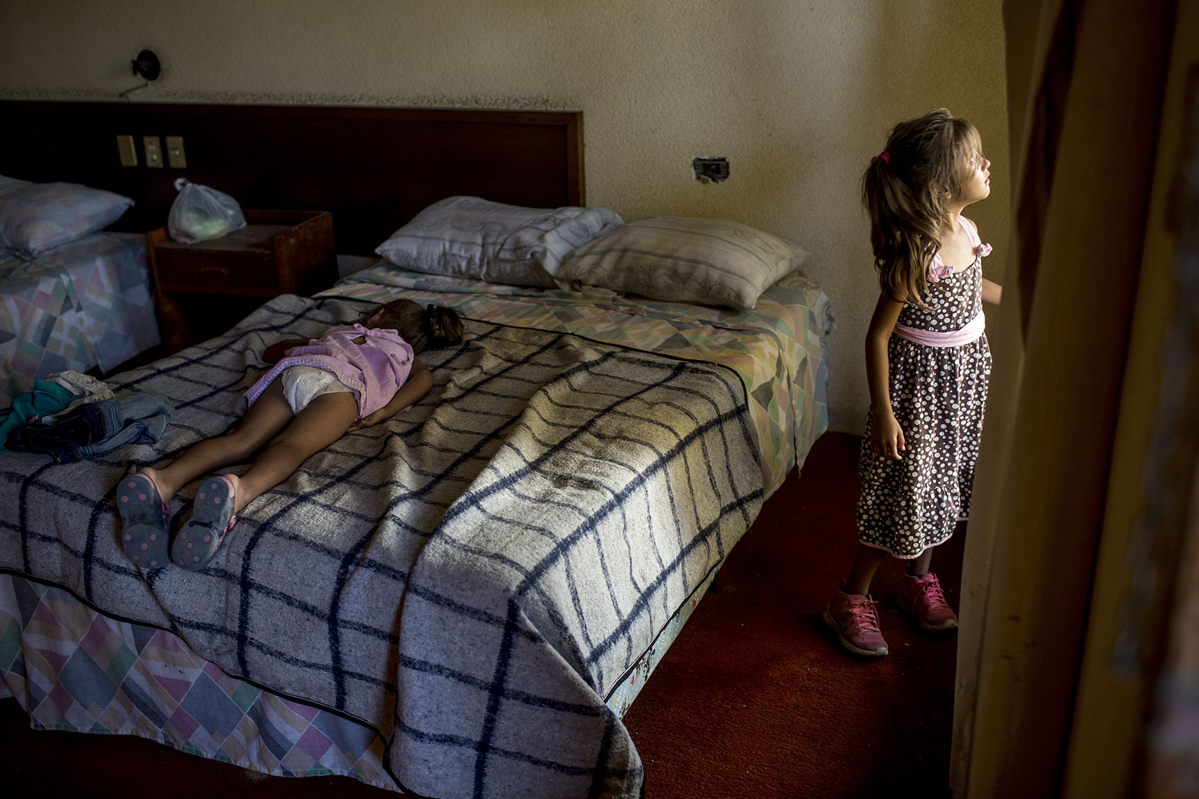Astrid Melara, 6, mira desde la ventana de un cuarto del hotel, donde pasará la noche con su hermana Nicole, 5, ya dormida encima de la cama / Simone Dalmasso