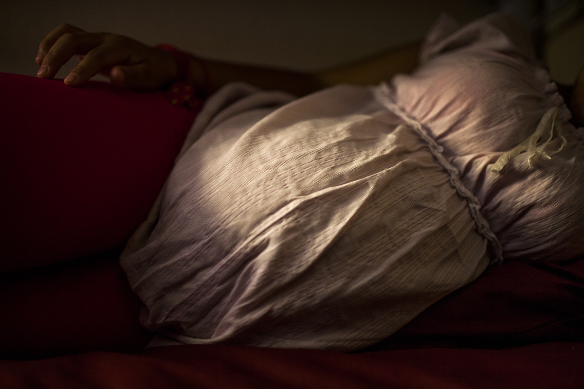 Una niña de 13 años escucha las preguntas acostada en su cama. En pocos días nacerá su hija.