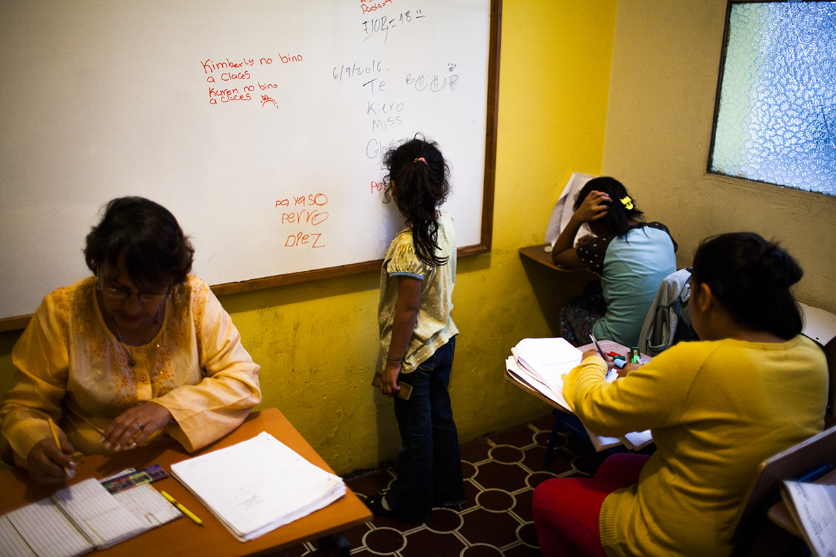 Una niña de seis años practica caligrafía en el pizarrón de la escuela del hogar, mientras sus compañeras estudian. 